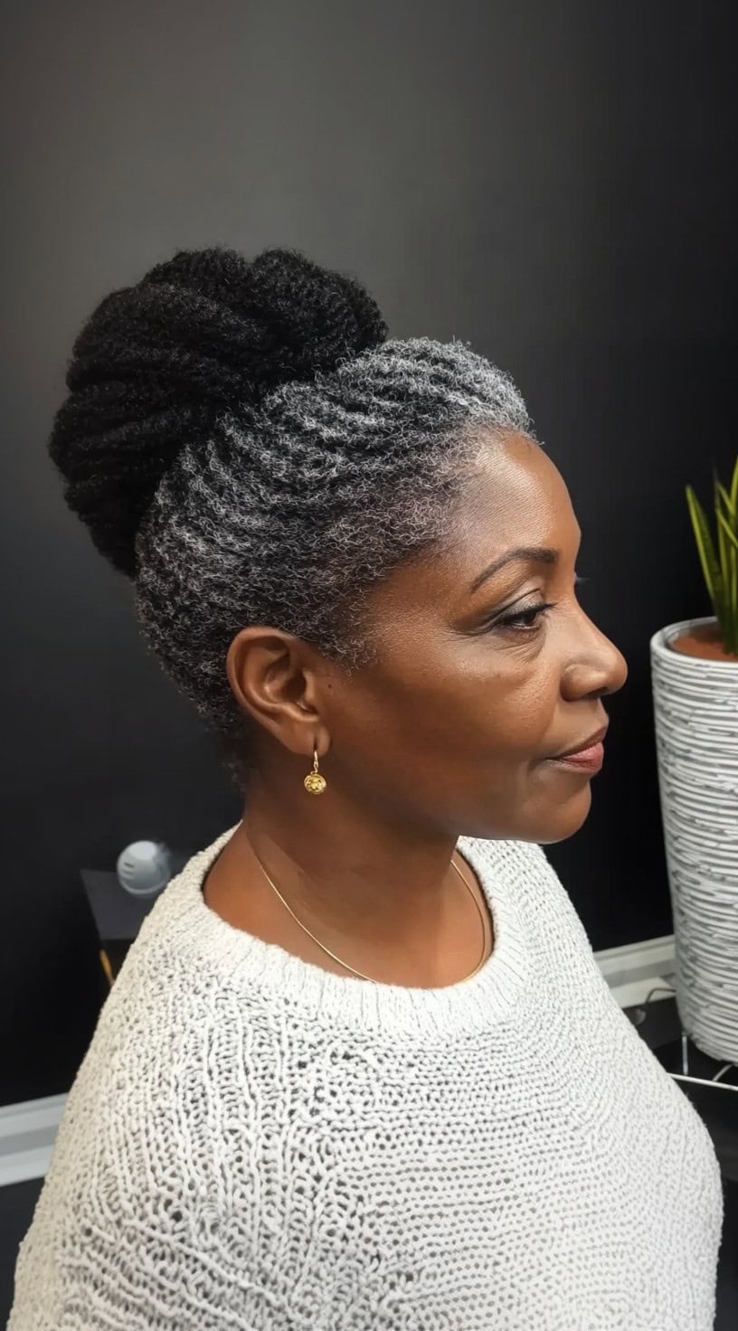 A side-profile view of an older Black woman with salt-and-pepper hair styled in an elegant twisted updo with a voluminous bun at the back.