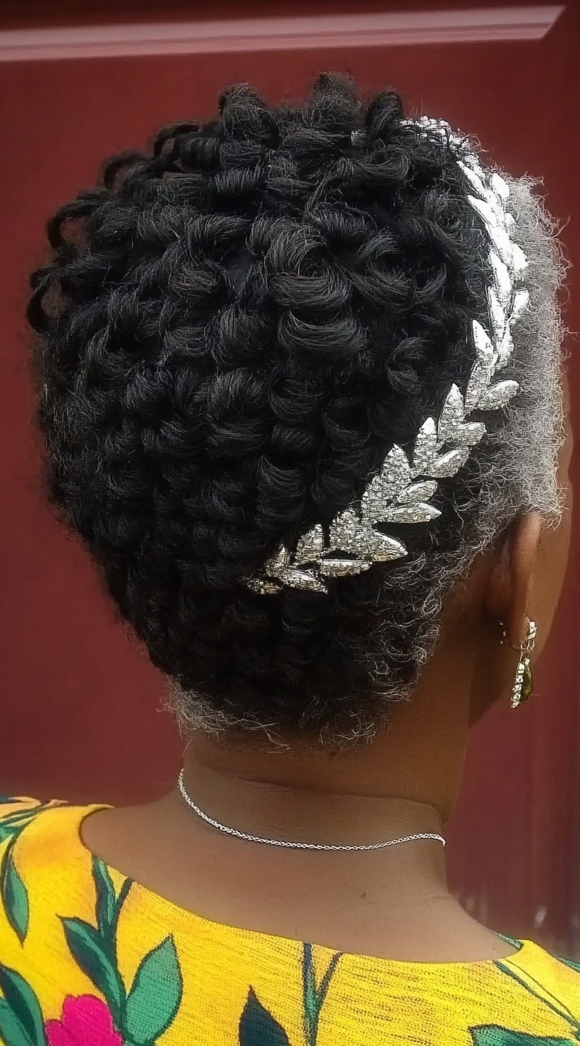 A close-up back view of a Black woman with intricately twisted flat twists styled into an updo, adorned with a silver leaf-shaped crystal headpiece.