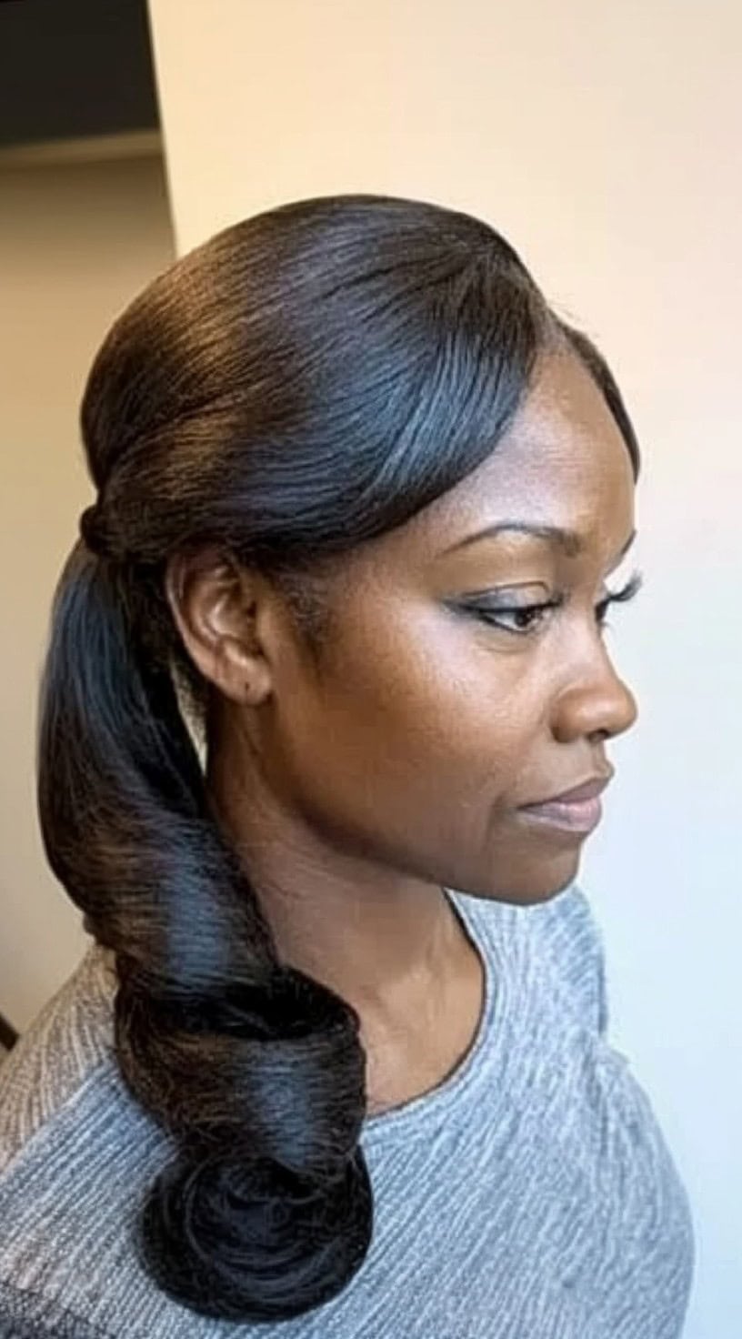 A side-profile view of a Black woman with a sleek, side-parted ponytail, featuring curled ends for a polished finish.