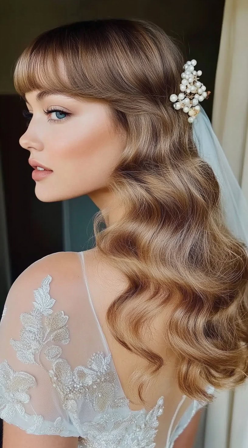 A woman with glossy, vintage Hollywood waves and full blunt bangs, adorned with pearl hair accessories and a bridal veil.